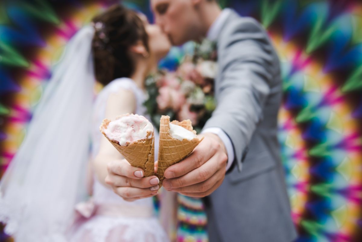 The bride and groom are eating ice cream together on a bright wall background.